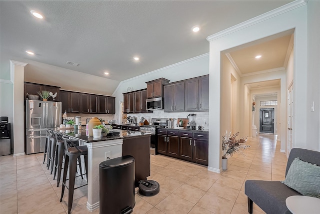 kitchen featuring light tile patterned flooring, dark brown cabinetry, visible vents, a kitchen breakfast bar, and appliances with stainless steel finishes