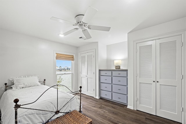 bedroom featuring baseboards, visible vents, a ceiling fan, dark wood-style flooring, and multiple closets