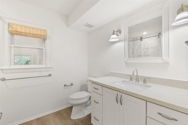 bathroom featuring toilet, wood finished floors, vanity, visible vents, and a shower