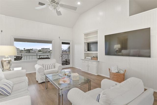 living area with built in features, lofted ceiling, a ceiling fan, and wood finished floors