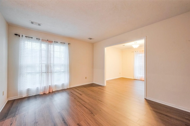 spare room with baseboards, a textured ceiling, visible vents, and wood finished floors