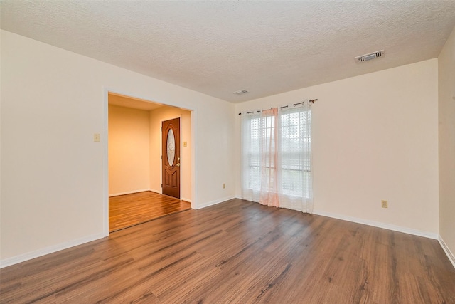 unfurnished room featuring baseboards, a textured ceiling, visible vents, and wood finished floors