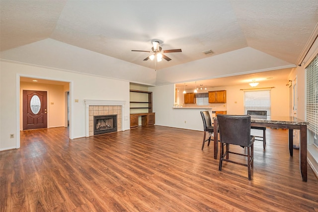 living area with a fireplace, visible vents, vaulted ceiling, and dark wood-type flooring