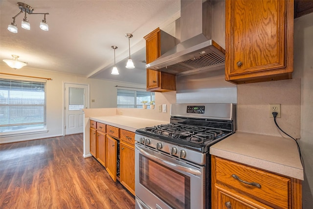 kitchen featuring stainless steel gas stove, wall chimney exhaust hood, brown cabinets, and a wealth of natural light