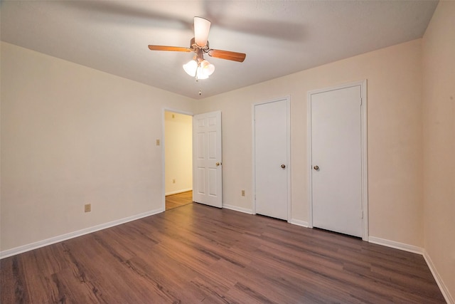 unfurnished bedroom featuring dark wood-style floors, ceiling fan, baseboards, and multiple closets