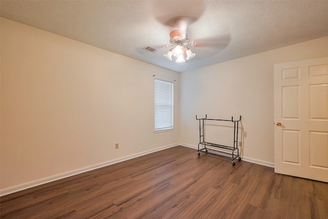 spare room with dark wood finished floors, visible vents, a ceiling fan, a textured ceiling, and baseboards