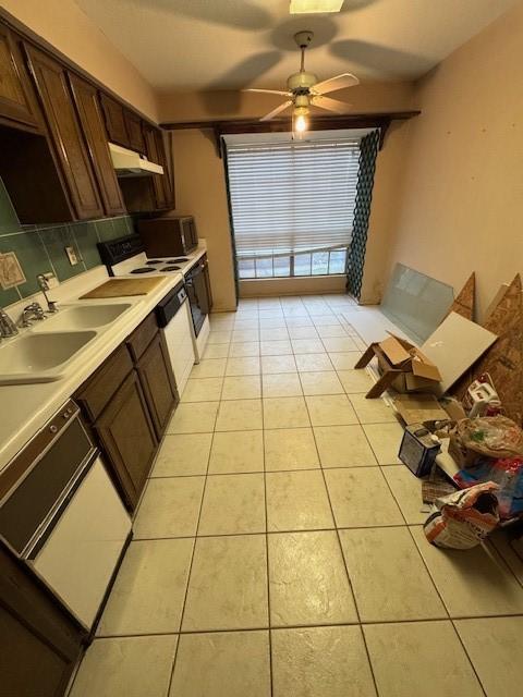 kitchen featuring backsplash, under cabinet range hood, light countertops, light tile patterned floors, and a sink