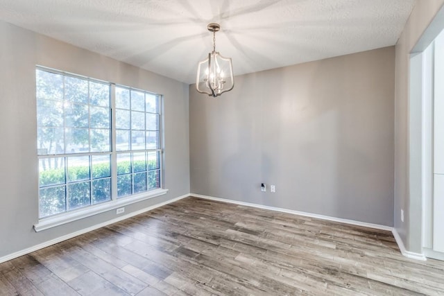 empty room featuring a notable chandelier, baseboards, and wood finished floors