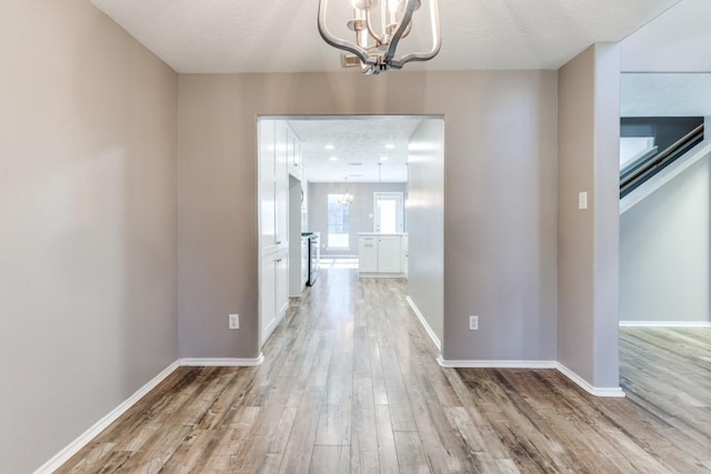 unfurnished dining area featuring baseboards, light wood-style floors, and a notable chandelier