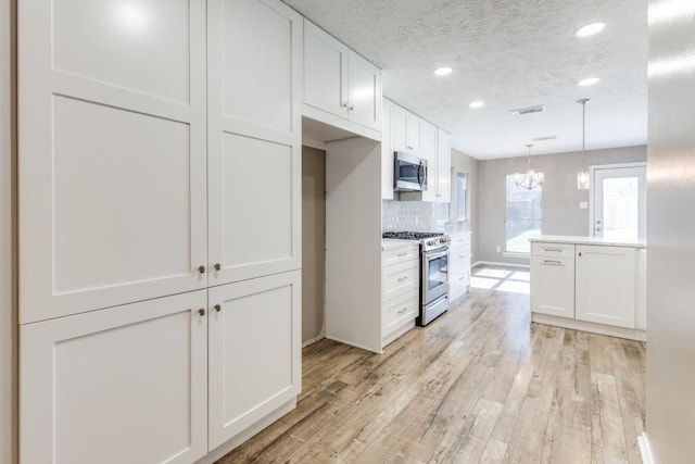 kitchen with a textured ceiling, stainless steel appliances, white cabinetry, decorative backsplash, and light wood finished floors