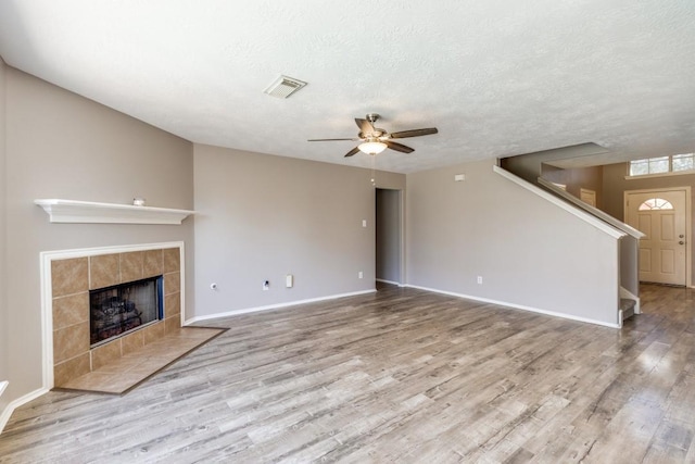 unfurnished living room featuring stairs, visible vents, a tiled fireplace, and wood finished floors