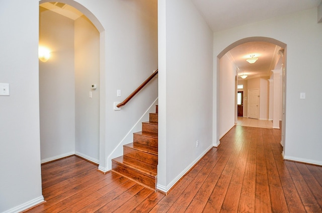 hallway with arched walkways, wood-type flooring, and baseboards