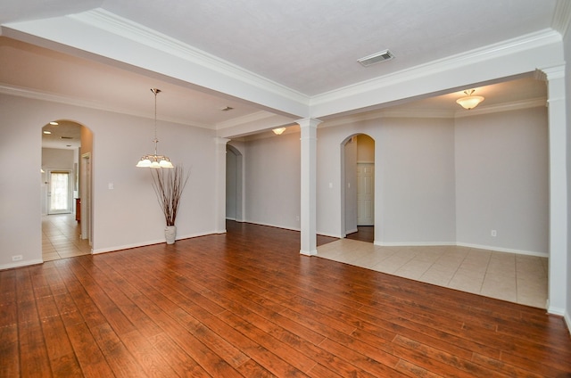 empty room with ornamental molding, arched walkways, visible vents, and hardwood / wood-style flooring