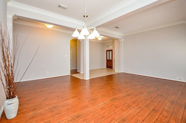 unfurnished room with decorative columns, visible vents, arched walkways, wood-type flooring, and crown molding