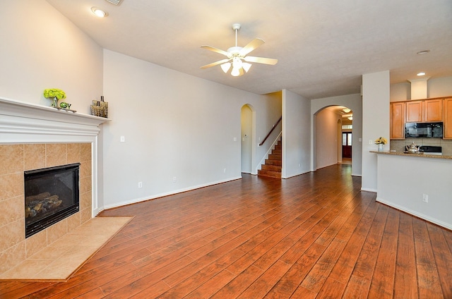 unfurnished living room featuring arched walkways, a fireplace, dark wood-type flooring, a ceiling fan, and baseboards