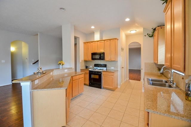 kitchen featuring arched walkways, range with gas cooktop, backsplash, a sink, and black microwave