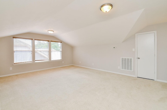 additional living space featuring light colored carpet, visible vents, vaulted ceiling, and baseboards