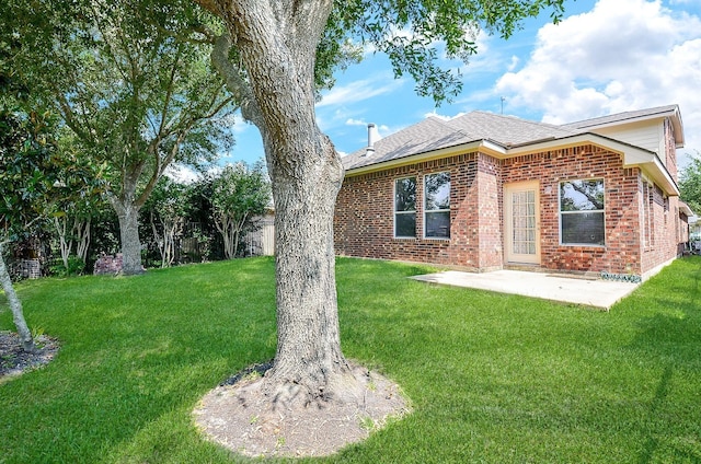 exterior space featuring a patio, brick siding, a front lawn, and roof with shingles