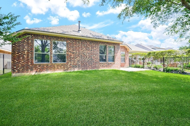 rear view of house featuring a yard, a shingled roof, fence, and brick siding