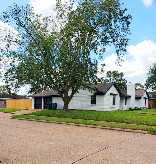 view of front facade with an attached garage, brick siding, driveway, a front lawn, and a chimney