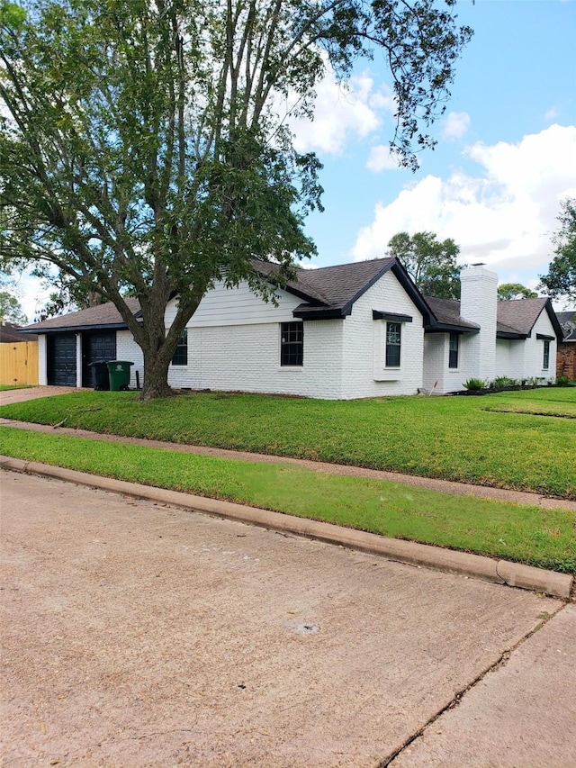 view of property exterior with an attached garage, brick siding, a yard, driveway, and a chimney