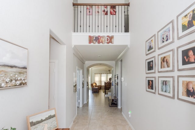 hall with baseboards, a high ceiling, arched walkways, and light tile patterned flooring