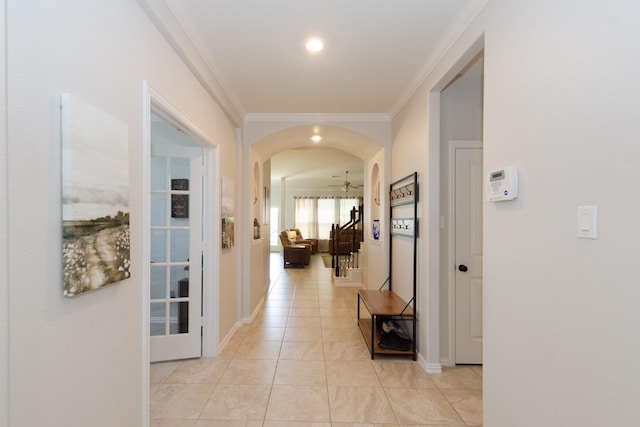 hallway featuring ornamental molding, arched walkways, baseboards, and light tile patterned floors