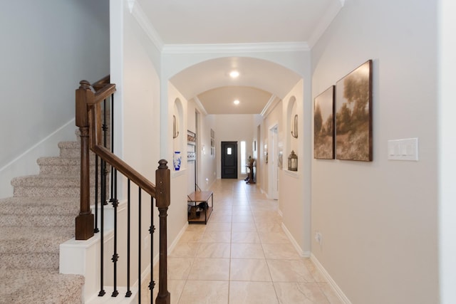 hallway featuring ornamental molding, arched walkways, baseboards, and light tile patterned floors