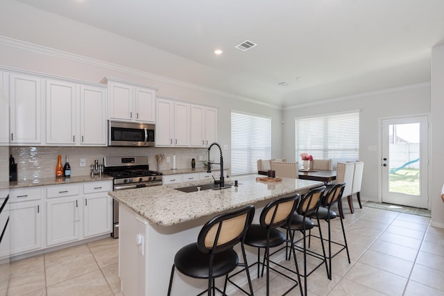 kitchen with a center island with sink, a sink, stainless steel appliances, crown molding, and backsplash