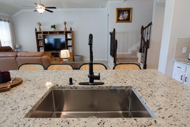 kitchen featuring ceiling fan, a sink, open floor plan, ornamental molding, and light stone countertops