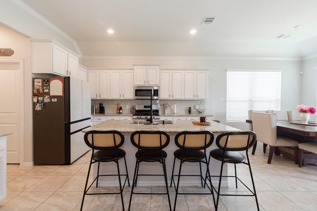 kitchen with tasteful backsplash, white cabinets, appliances with stainless steel finishes, a breakfast bar area, and light tile patterned flooring