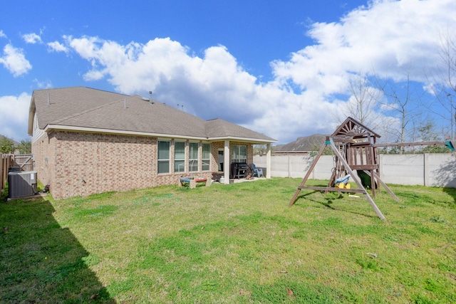 back of property featuring a playground, a yard, brick siding, central AC, and a fenced backyard