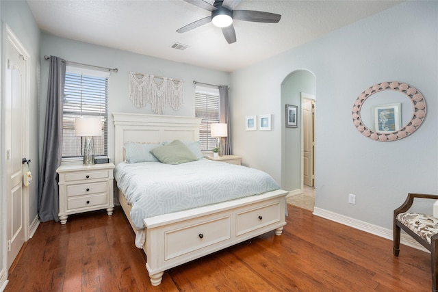 bedroom with baseboards, visible vents, a ceiling fan, arched walkways, and dark wood-style flooring