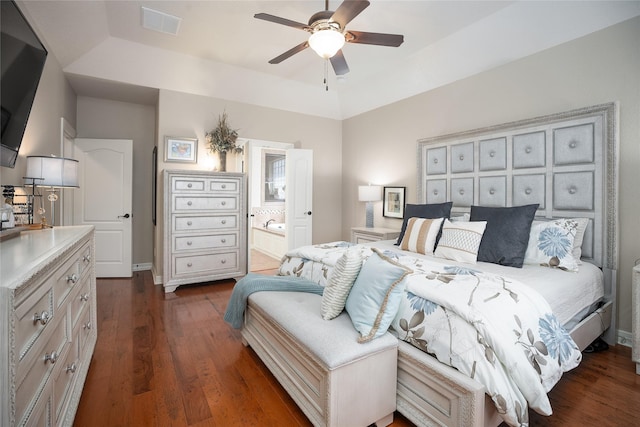 bedroom with a raised ceiling, visible vents, ensuite bathroom, dark wood-type flooring, and a ceiling fan