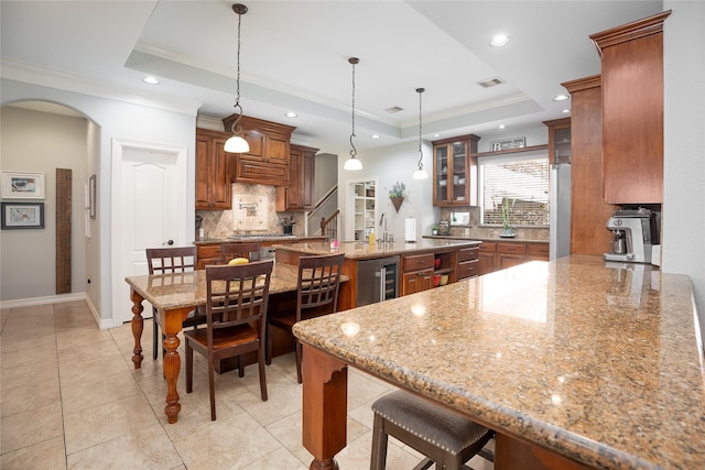 kitchen with beverage cooler, a tray ceiling, a breakfast bar, and arched walkways