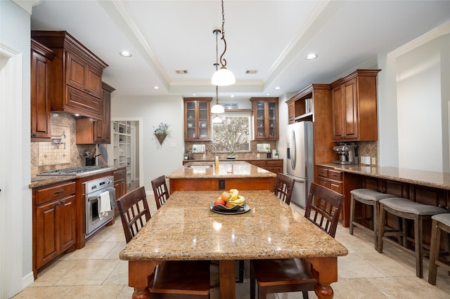 kitchen with stainless steel appliances, a raised ceiling, a kitchen island with sink, and a breakfast bar area