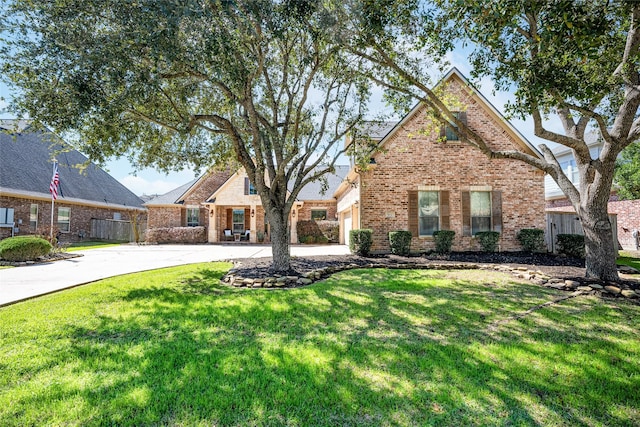 traditional-style house featuring concrete driveway, brick siding, a front lawn, and fence