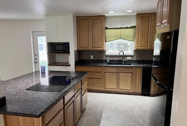 kitchen featuring a textured ceiling, a sink, decorative backsplash, dark stone counters, and black appliances