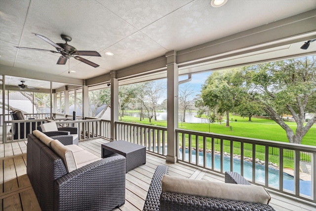 wooden deck featuring a water view, an outdoor living space, a ceiling fan, a lawn, and an outdoor pool