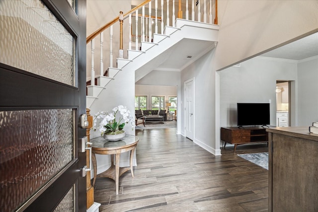 entrance foyer with ornamental molding, a towering ceiling, baseboards, and wood finished floors