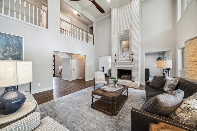 living room featuring a fireplace, a towering ceiling, a ceiling fan, wood finished floors, and baseboards