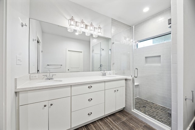 full bath featuring double vanity, a shower stall, a sink, and wood finished floors