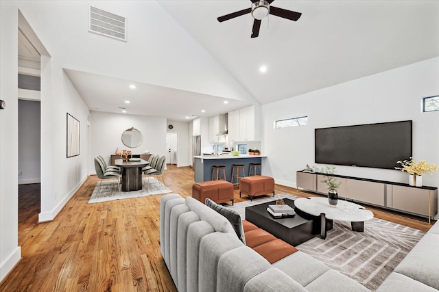 living area with visible vents, baseboards, ceiling fan, light wood-style floors, and high vaulted ceiling