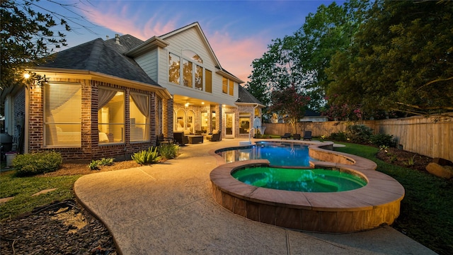 pool at dusk with a fenced in pool, a fenced backyard, a patio, and an in ground hot tub