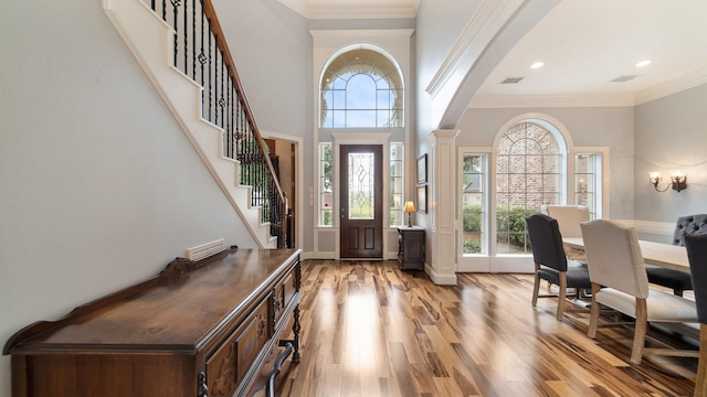 foyer with crown molding, light wood finished floors, visible vents, ornate columns, and stairs