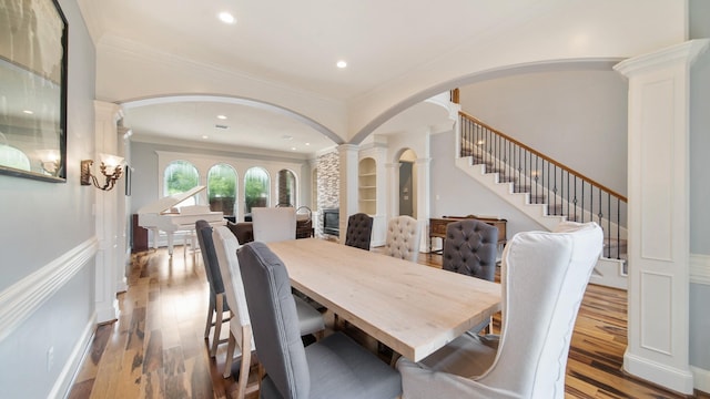 dining area with ornamental molding, arched walkways, ornate columns, and wood finished floors