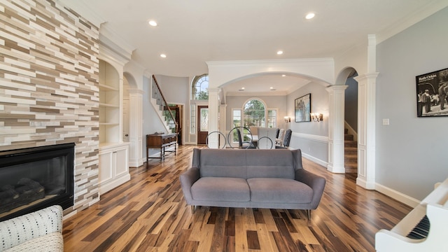 living room with built in features, crown molding, decorative columns, stairway, and wood finished floors