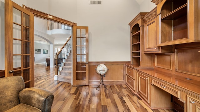 home office with arched walkways, a wainscoted wall, wood finished floors, visible vents, and decorative columns