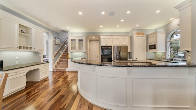 kitchen with dark stone counters, wood finished floors, black appliances, open shelves, and built in desk