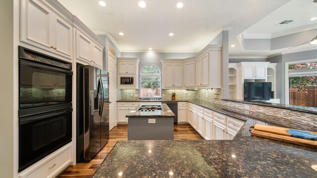 kitchen featuring a center island, decorative backsplash, dark stone countertops, light wood-type flooring, and black appliances